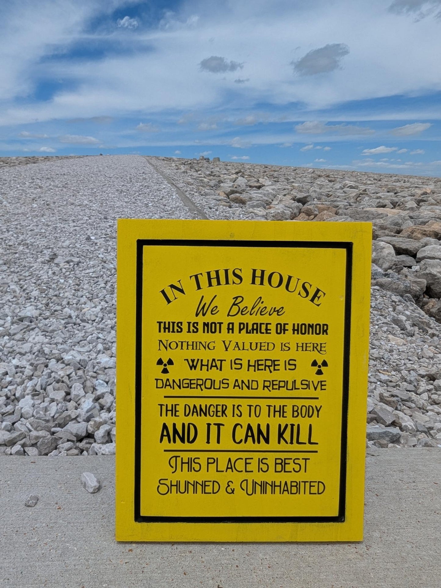A 12 by 9 inch sign that says In this house we believe this is not a place of honor. Nothing valued is here. What is here is dangerous and repulsive, the danver is to the body and it can kill. This place is best Shunned and uninhabited. Black lettering on yellow background