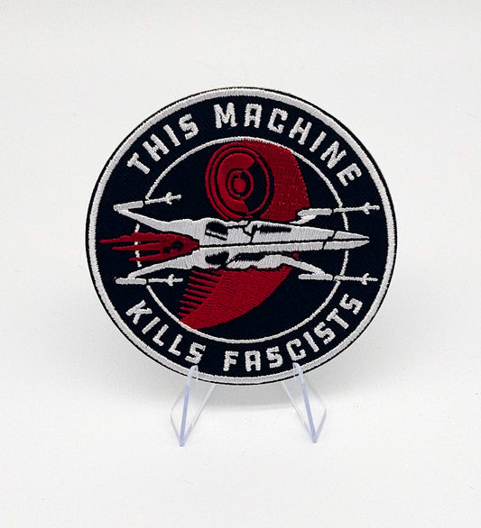 Patch with text 'This machine kills fascists' on a stand against a white background