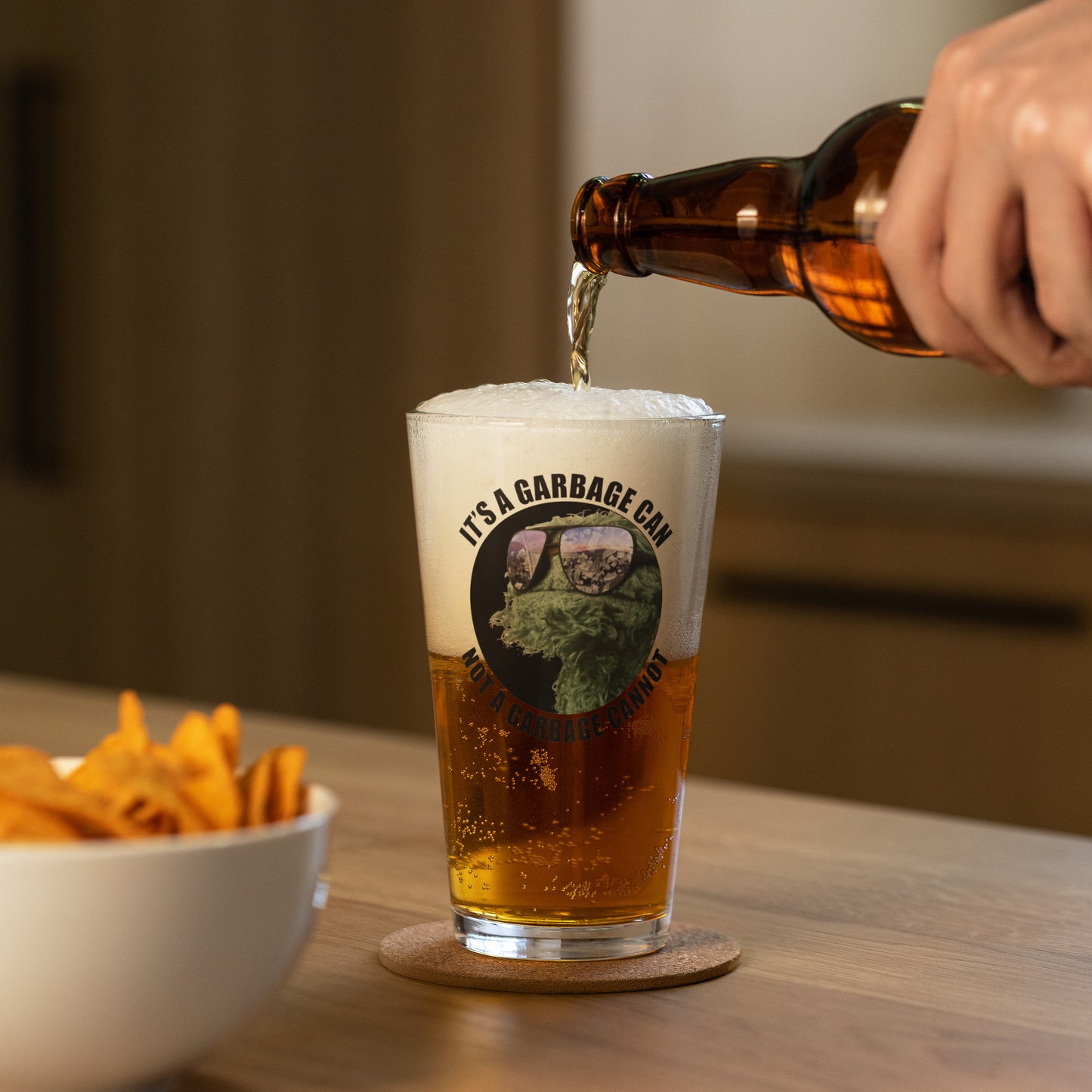 Pint Glass with circle lettering reading It's a  Garbage Can, not a Garbage Cannot in a circle. with Oscar the grouch in the center. 